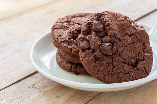Soft baked dark chocolate cookies in white plate on wooden table